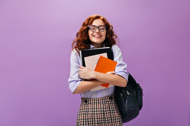 Free photo curly girl in eyeglasses holds notebooks on purple wall