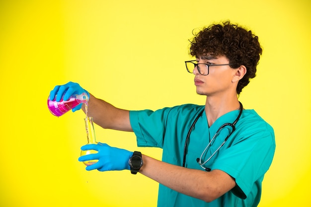 Curly hair boy in medical uniform and hand masks doing chemical reaction in attentive manner.