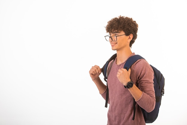 Curly hair boy in optique glasses holding his backpack is confident and motivated.