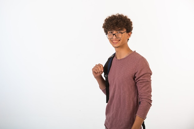 Curly hair boy in optique glasses holding his backpack and is ready for education.