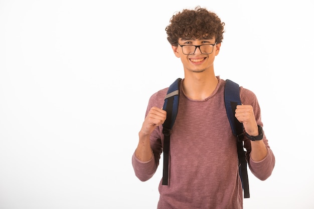 Curly hair boy in optique glasses holding his backpack and is ready for travel.