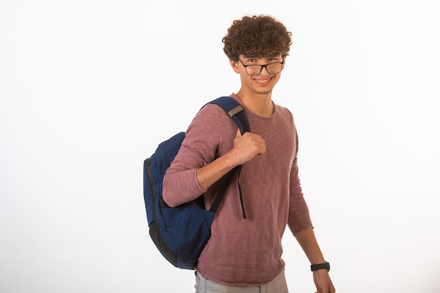 Curly hair boy in optique glasses holding his backpack and smiling.