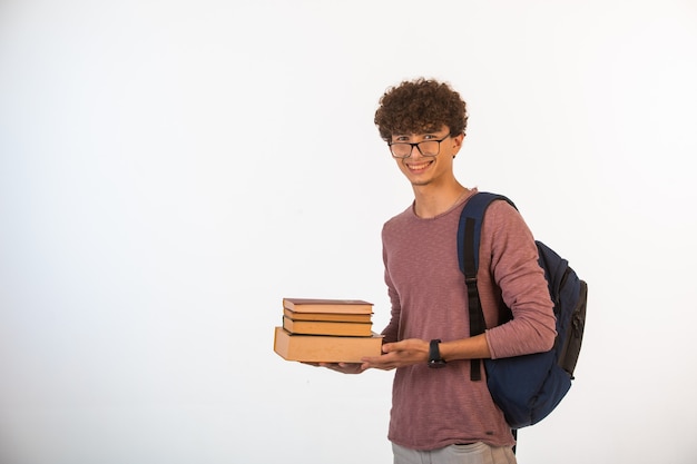 Curly hair boy in optique glasses holding school books, smiling and is focused.