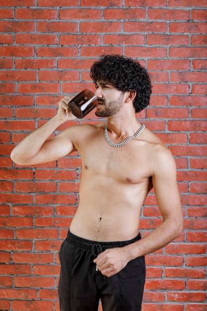 Curly haired half naked man drinkng cup of tea.