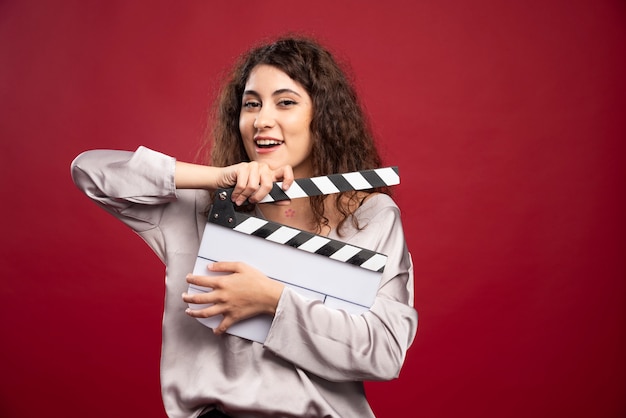 Curly haired woman holding clapperboard.