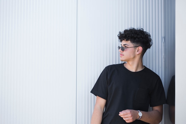 Curly man in glasses looking away at gray fence