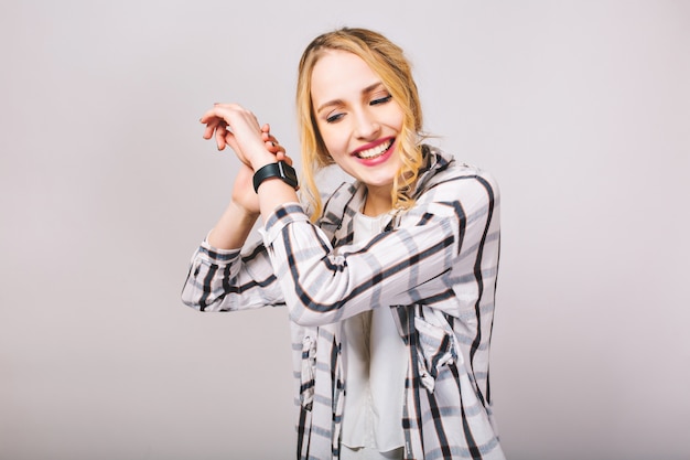 Free Photo curly pretty girl in striped trendy shirt listens with interest to the ticking of new black wristwatch. smiling attractive fair-haired young woman posing with hands up isolated.