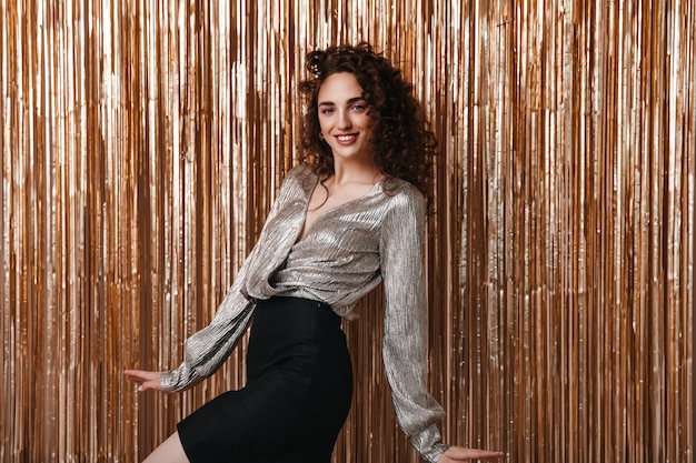 Curly woman in festive outfit smiling on gold background