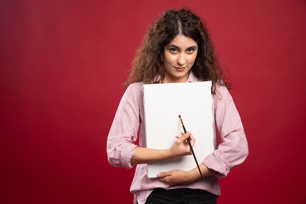 Curly woman holding paintbrush and canvas.