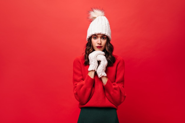 Curly woman in red sweater, knitted hat and mittens looks at front