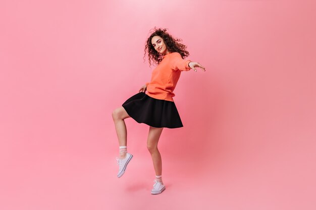 Curly woman in stylish outfit dancing on pink background