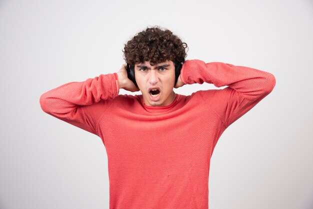 Curly young man listening to song and screaming.