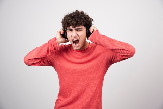 Curly young man with headphones listening to song with loud volume.