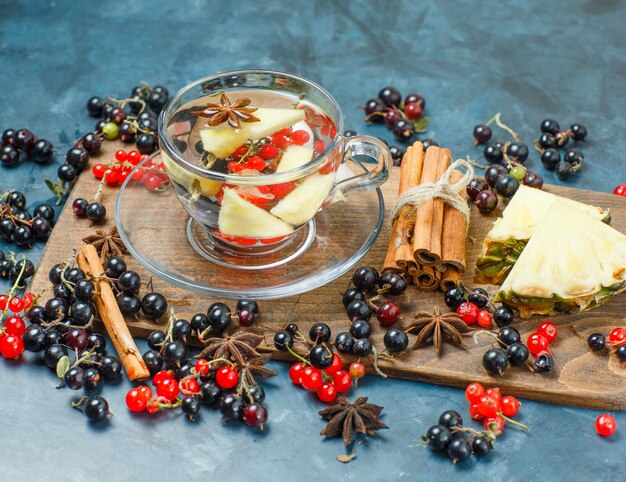 Currants with spices, pineapple, drink high angle view on dark blue and cutting board