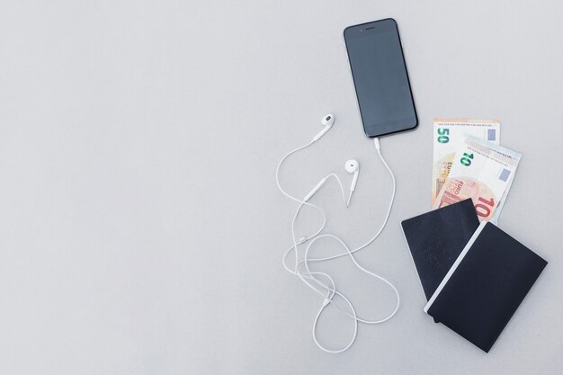 Currency note in the passport with cellphone and earphone on gray backdrop