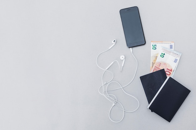 Currency note in the passport with cellphone and earphone on gray backdrop