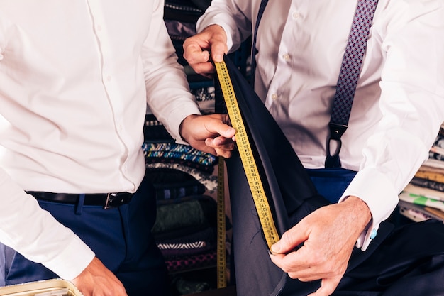 Free photo customer and senior male tailor measuring the fabric with yellow measure table