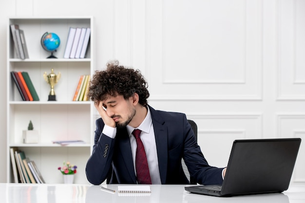 Customer service curly brunette young man in office suit and red tie with laptop tired