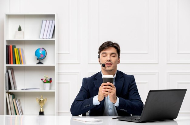 Customer service handsome guy with headset and laptop in suit closing eyes and holding a coffee