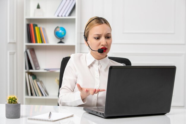 Customer service pretty blonde girl in white shirt with laptop and headset annoyed on a videocall