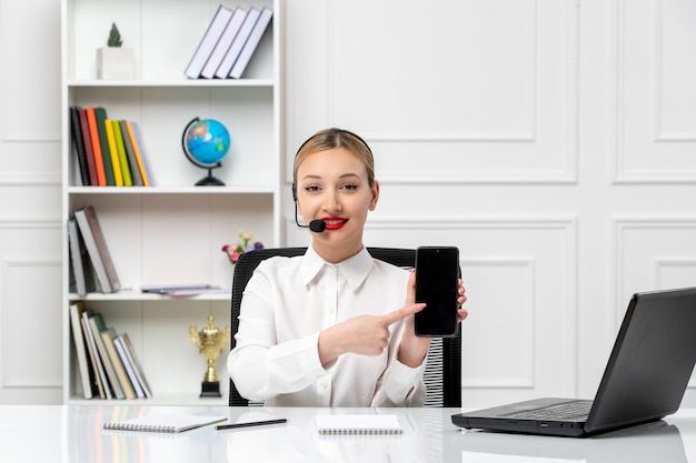 Customer service pretty blonde girl in white shirt with laptop and headset smiling with phone