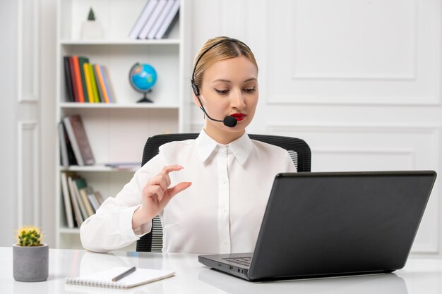 Customer service pretty blonde girl in white shirt with laptop and headset on the videocall