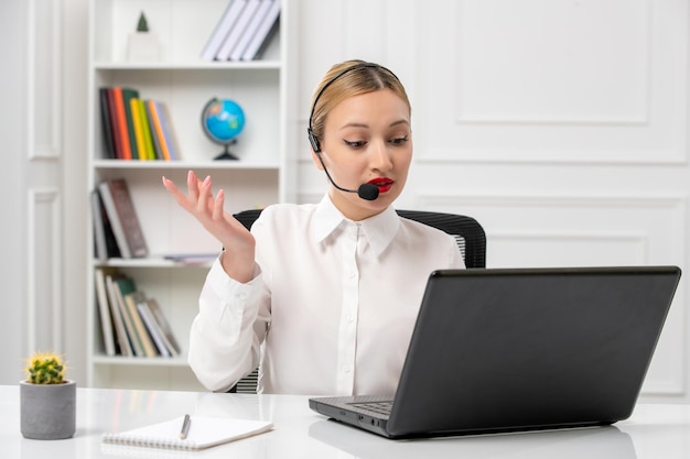 Customer service pretty blonde girl in white shirt with laptop and headset waving hands