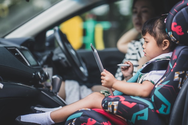 Cute Asian small girl sitting in a car with her mom and watching cartoons