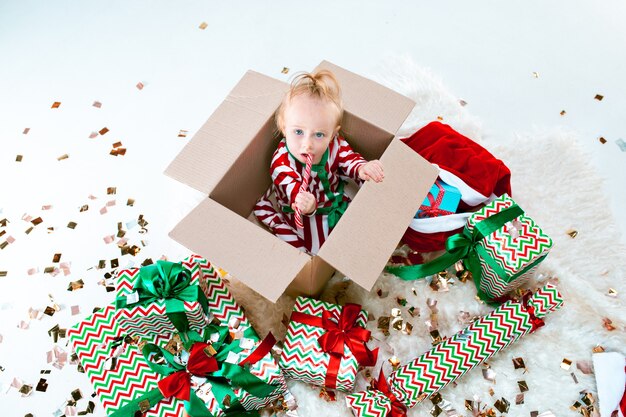 Cute baby girl 1 year old sitting in box over Christmas decoration background. Holiday, celebration, kid concept