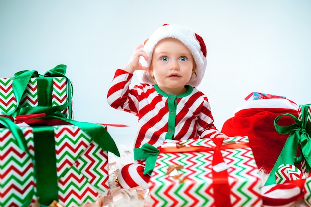 Cute baby girl near santa hat posing over Christmas background with decoration. Sitting on floor with Christmas ball.