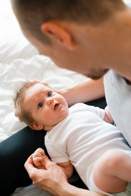 Free Photo cute baby laying on knees of dad