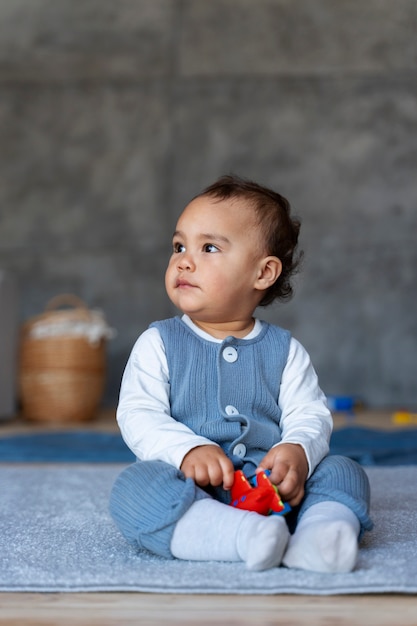 Free photo cute baby playing with toy while sitting on the floor