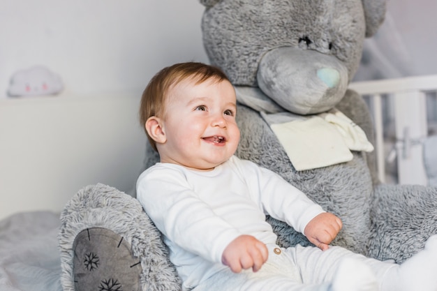 Cute blonde baby in white bed with teddy bear