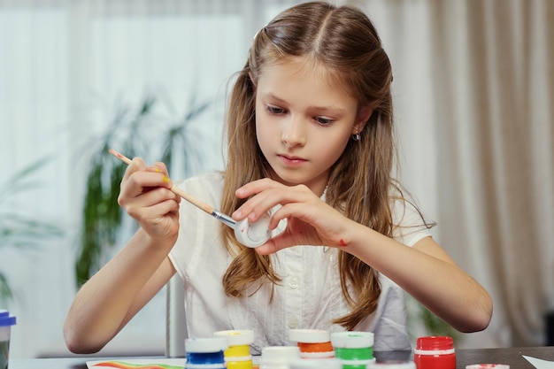 Cute blonde girl painting with acrylic paint in art studio class.