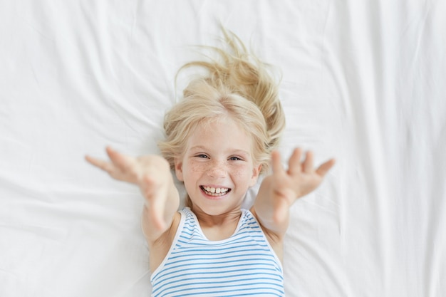 Cute blonde little girl stretching in white bed