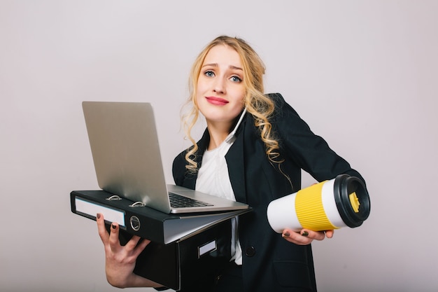 Cute blonde young office woman in white shirt, black jacket, with laptop, folder, coffee to go isolated. Expressing true emotions, success, work, having fun