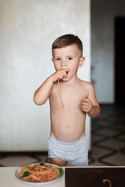 Cute boy eating spaghetti with his hand