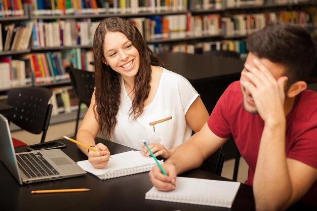 Cute brunette flirting and laughing with a friend she likes while studying in the library