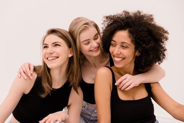 Free photo cute caucasian young blonde girl hugging her interracial girlfriends in black tops on white background beauty concept