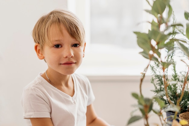 Cute child sitting next to plant at home