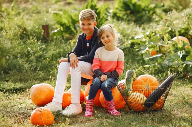 Cute childresn sitting on a garden near many pumpkins