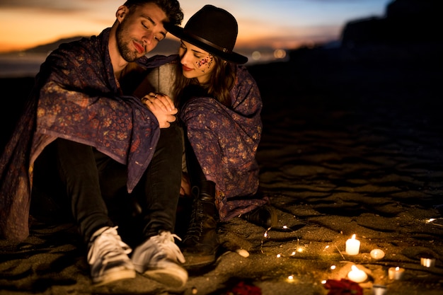 Free Photo cute couple in blanket sitting on sea shore