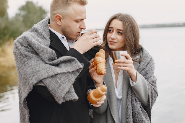 Cute couple in a park. Lady in a gray coat. People with a thermos and croissant.