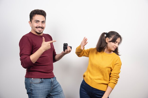 Cute couple taking pictures with camera and posing over a white wall.