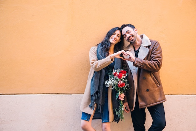 Cute couple with bouquet showing heart gesture