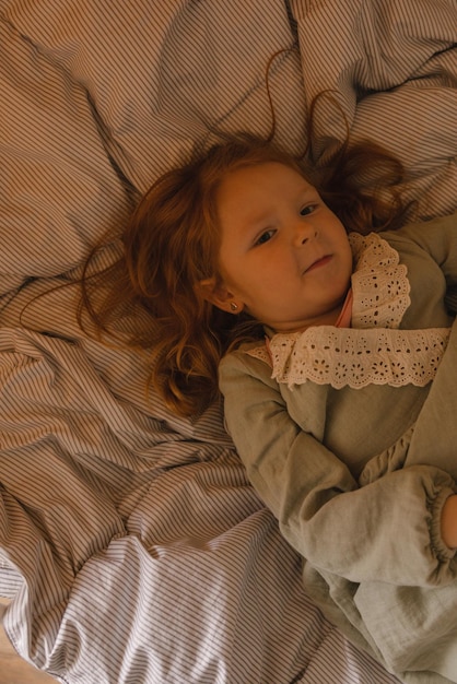 Free photo cute fairskinned little redhead girl child in casual clothes lies in bed at home baby girl concept