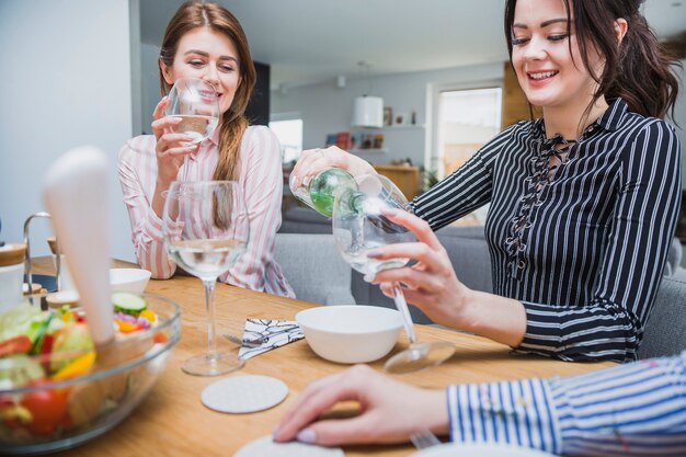 Cute female pouring white wine for friend