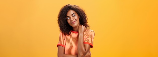 Free Photo cute and gentle dreamy darkskinned girl with cruly hairstyle tilting head smiling from delight and happiness touching neck tender gazing at upper left corner thinking or being nostalgic