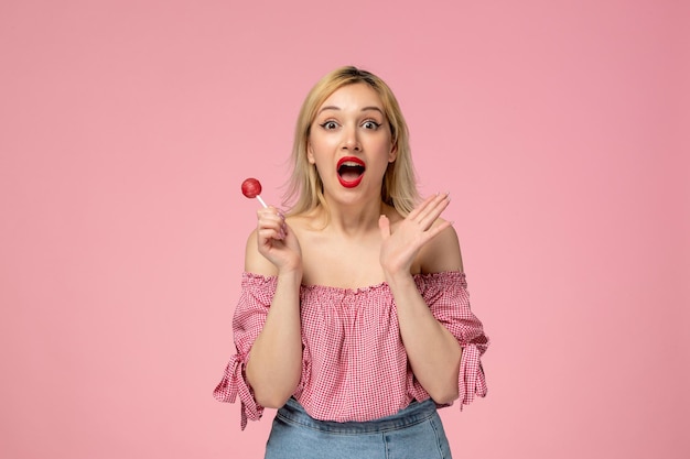 Cute girl adorable blonde chick with red lipstick in pink blouse so excited for a lollipop