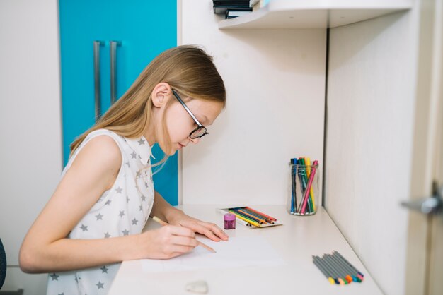 Cute girl drawing with pencil at table